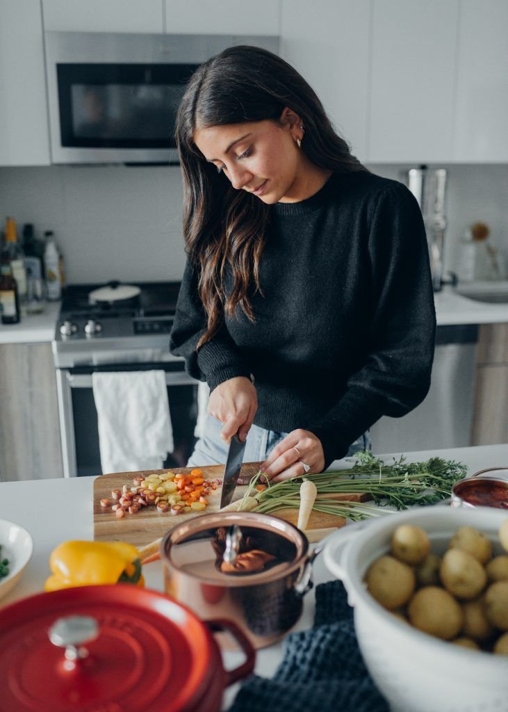 Woman chopping vegetables in a modern kitchen, preparing a meal with fresh ingredients on a wooden board.