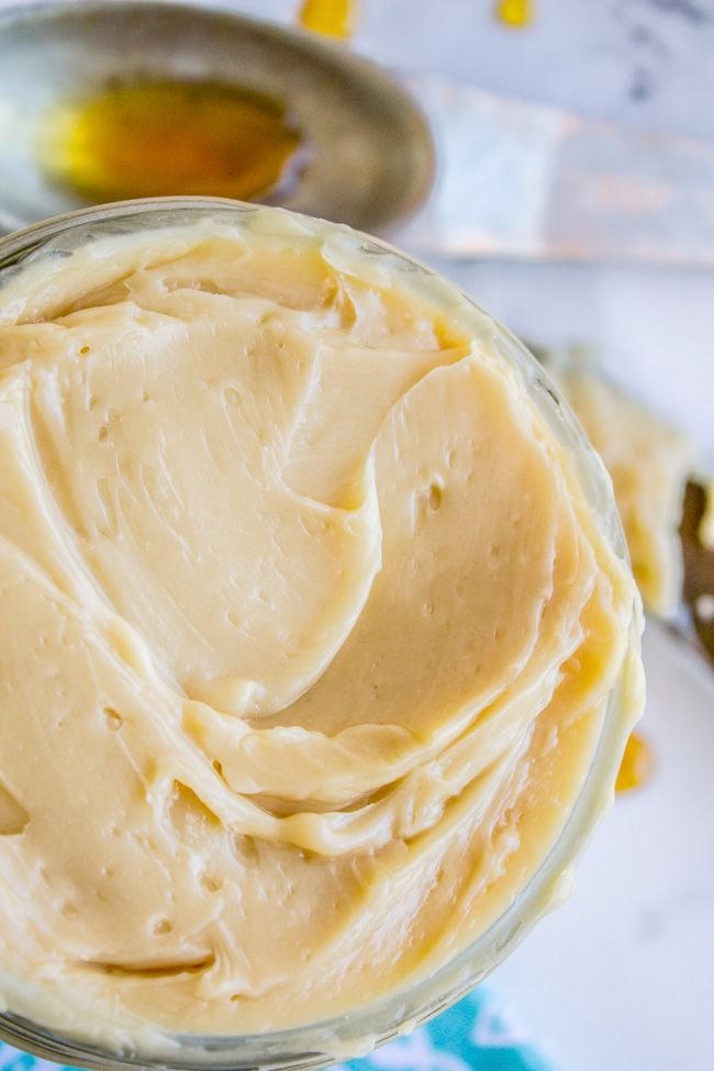 Creamy honey butter in a jar with a spoonful of honey beside it on a table.