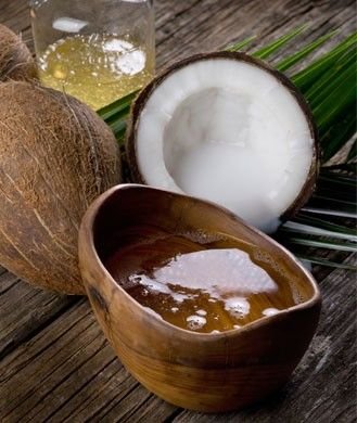 Fresh coconut oil in a wooden bowl surrounded by whole and halved coconuts on a rustic wooden surface.