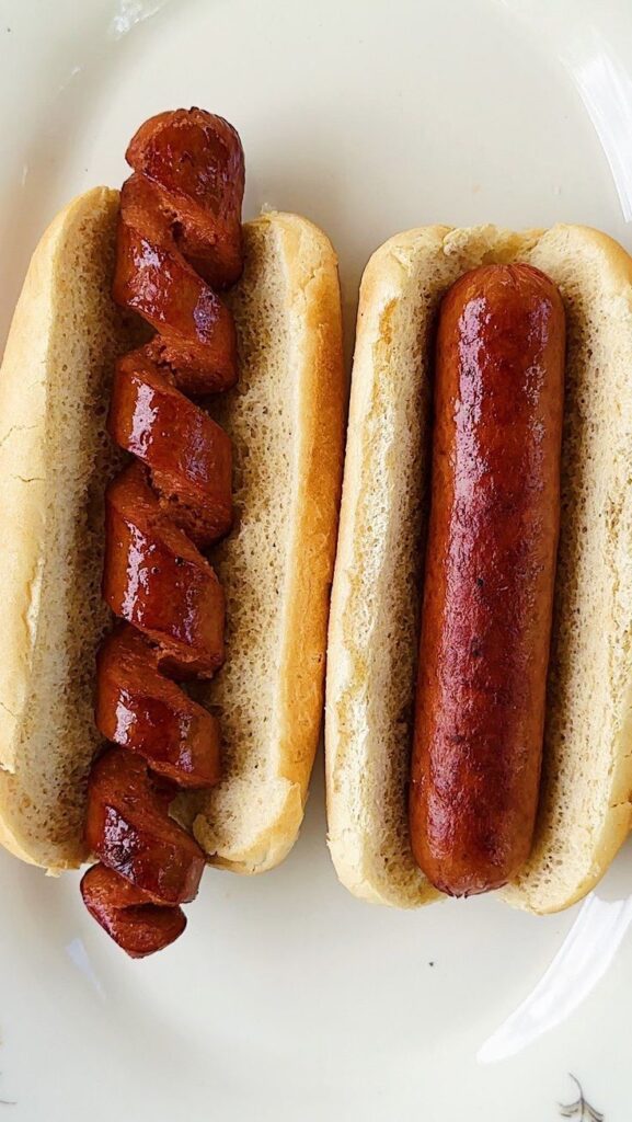 Two hot dogs in buns, one with a spiral cut sausage, showcasing a unique grilling style.