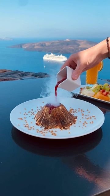 Pouring sauce over a dessert with a sea view and cruise ship in the background, Santorini dining experience.