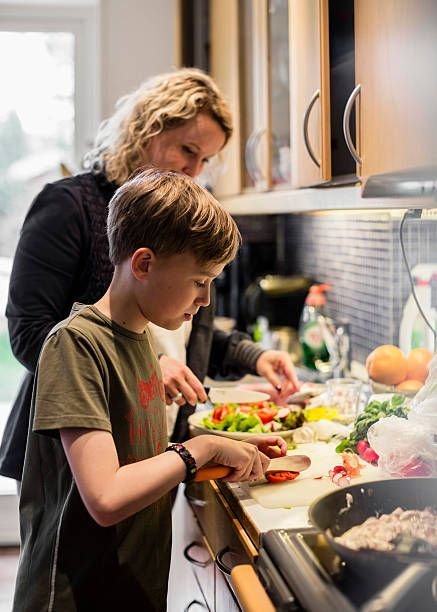 Young boy and woman chopping vegetables in a kitchen, preparing a healthy meal together.