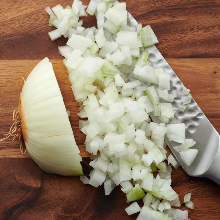 Chopped onions on a wooden board with a knife, perfect for cooking or recipe preparation.