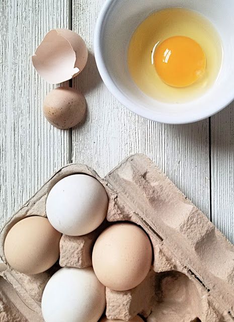 Fresh eggs in a carton with one cracked and yolk in a bowl on white wooden surface. Perfect for breakfast themes.