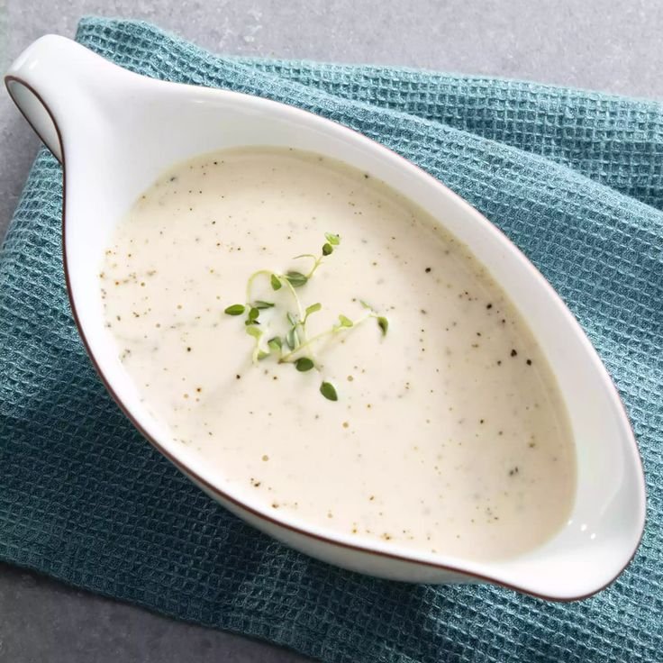 Creamy white sauce in a gravy boat garnished with fresh herbs, set on a blue cloth.