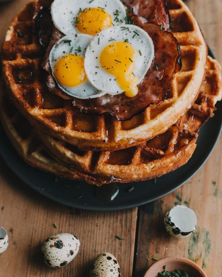 Delicious waffles topped with fried eggs and bacon, garnished with herbs. Perfect for a hearty breakfast.