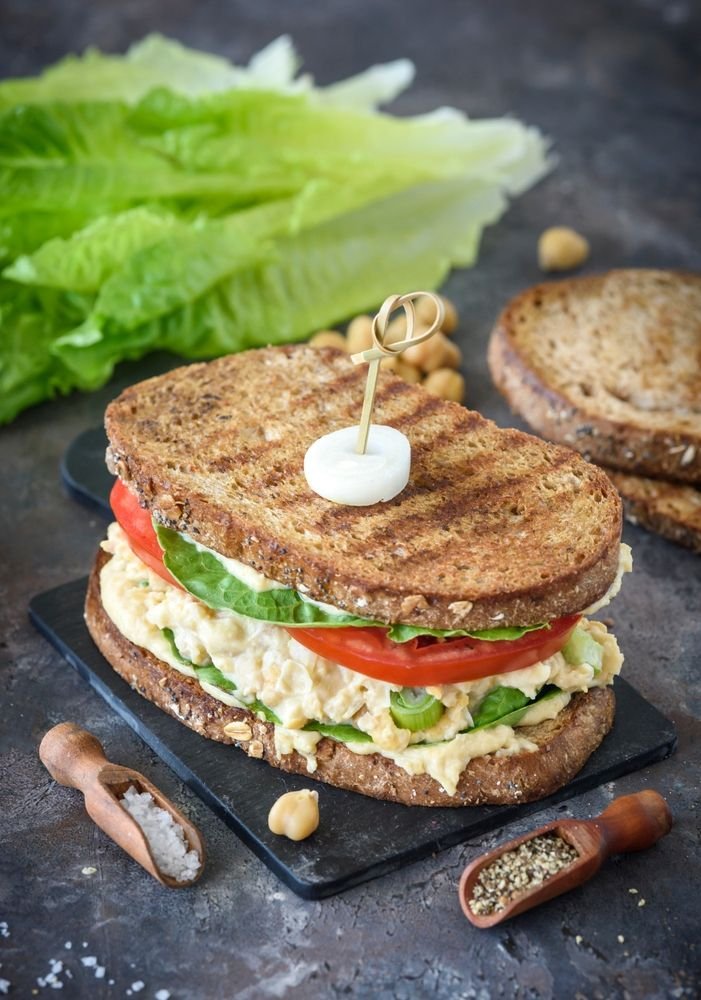 Healthy chickpea sandwich with lettuce and tomato on whole grain bread, garnished with spices.