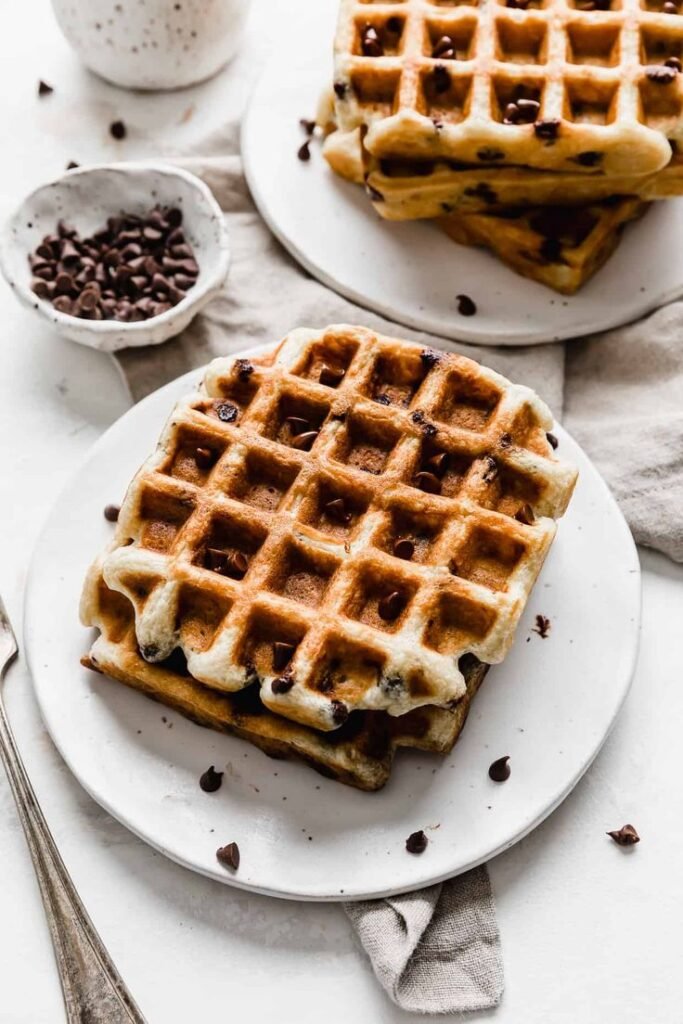 Delicious stack of chocolate chip waffles on a white plate, perfect for breakfast or brunch.