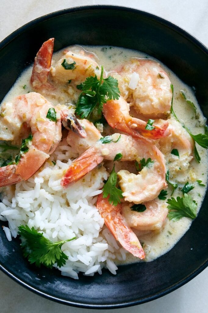 Creamy shrimp curry with white rice and cilantro garnish in a black bowl. Delicious seafood dish.