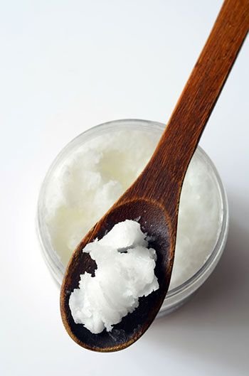 Wooden spoon with coconut oil over a jar, showcasing natural skincare ingredient.