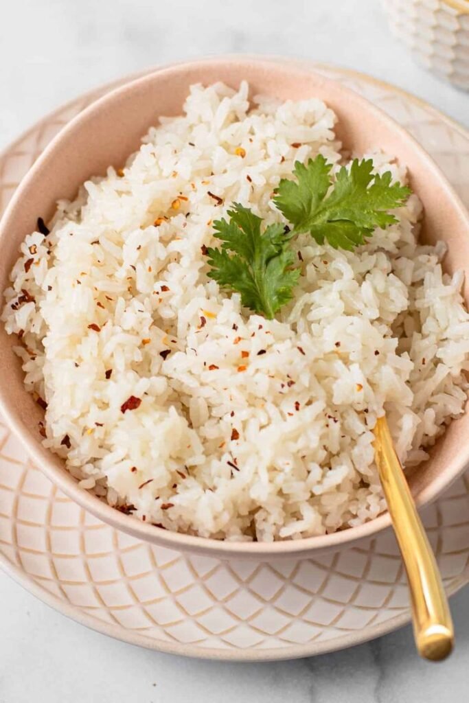 Bowl of fluffy white rice garnished with cilantro and chili flakes, served with a golden spoon on a patterned plate.