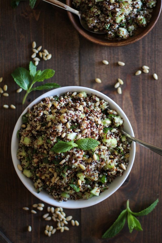Bowl of quinoa salad with fresh mint and pine nuts on a wooden table.