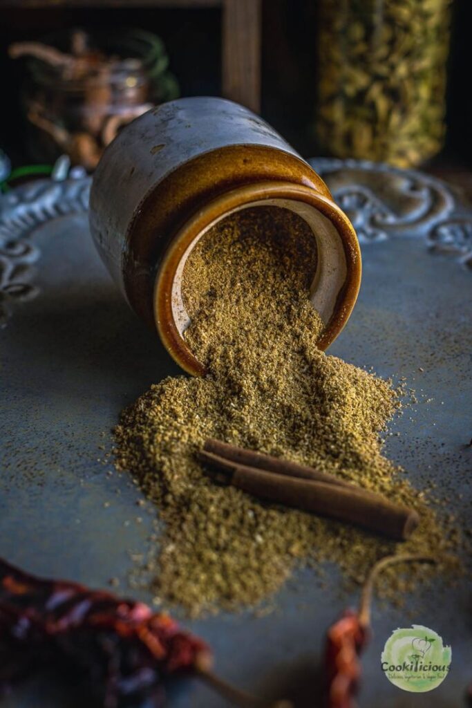 Spilled spice jar and cinnamon sticks on a decorative tray, highlighting aromatic flavors in rustic kitchen setting.
