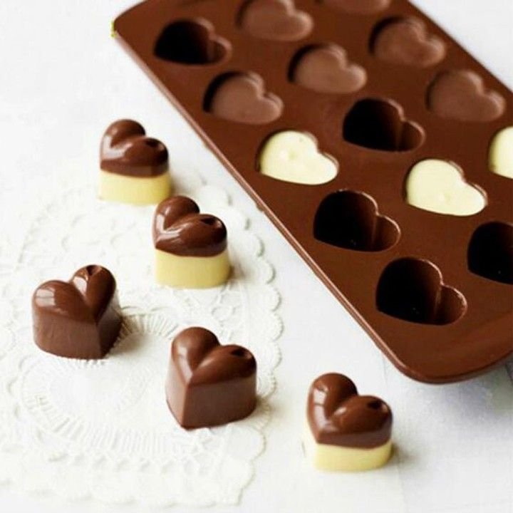 Heart-shaped chocolate candies on doily with silicone mold nearby, showcasing homemade sweet treats.