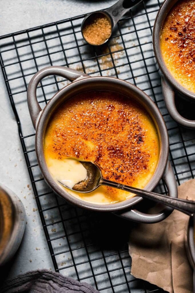 Creamy crème brûlée in a ceramic dish with a spoon, on a cooling rack, garnished with caramelized sugar topping.