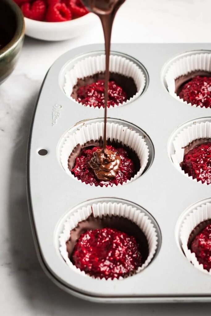 Pouring chocolate over raspberry filling in cupcake liners for a delicious dessert recipe.