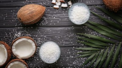 Coconuts and shredded coconut in bowls on dark wooden background with palm leaves.