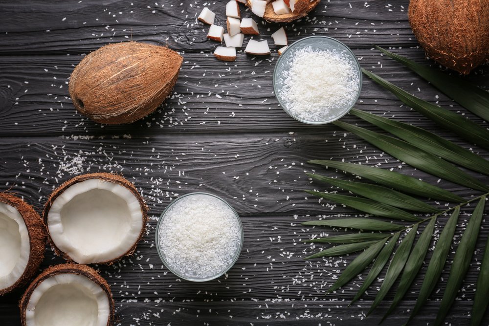 Coconuts and shredded coconut in bowls on dark wooden background with palm leaves.