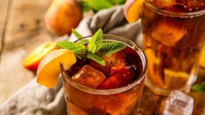 Refreshing iced tea with peach slices and mint leaves in a glass on a wooden table.