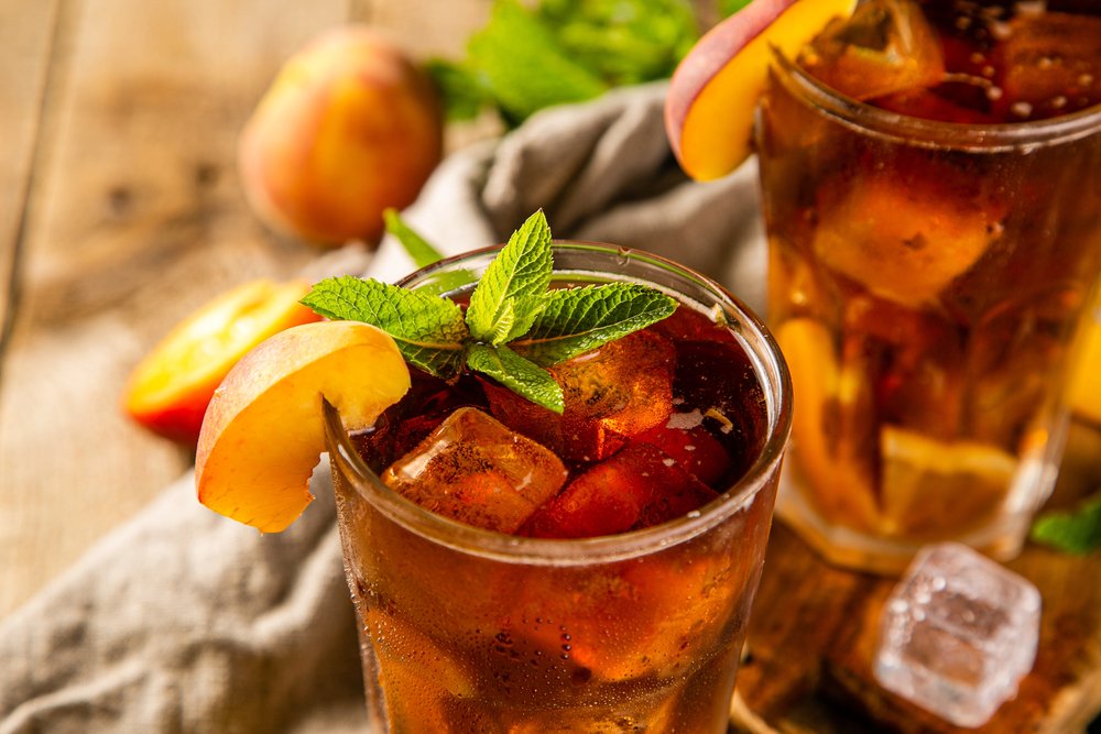 Refreshing iced tea with peach slices and mint leaves in a glass on a wooden table.