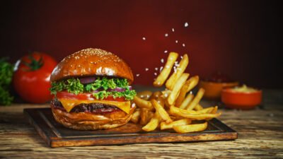 Juicy cheeseburger with fresh lettuce and tomato served with crispy fries, sprinkled with salt on a wooden tray.