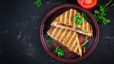 Grilled vegetable panini with tomato and herbs on a rustic plate, garnished with fresh parsley leaves.