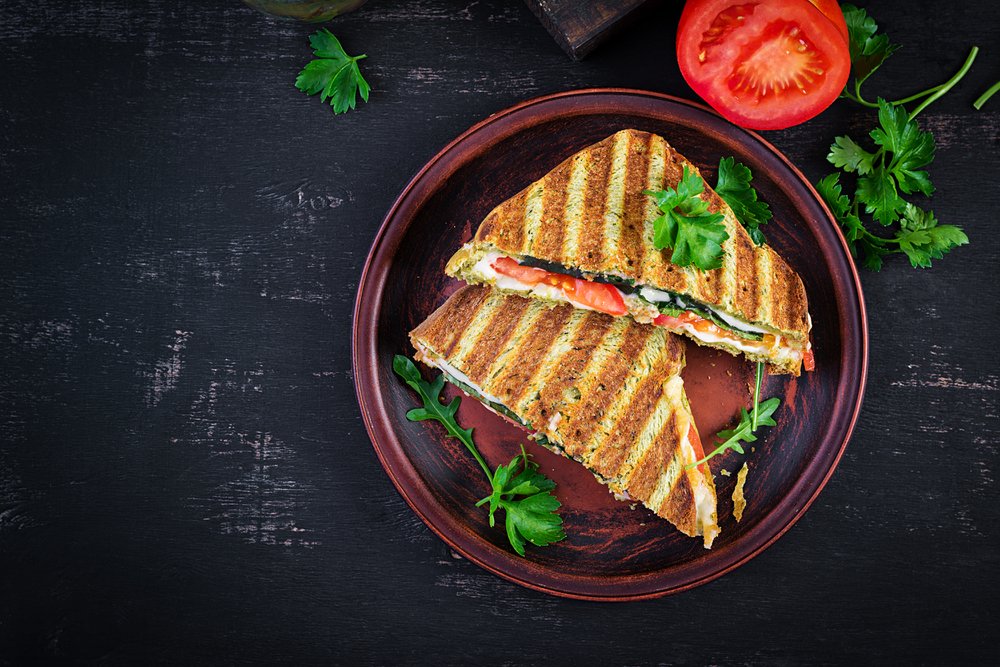 Grilled vegetable panini with tomato and herbs on a rustic plate, garnished with fresh parsley leaves.