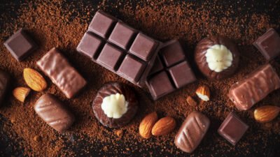 Assorted chocolate bars, truffles, and almonds on a bed of cocoa powder, creating a rich and indulgent treat scene.