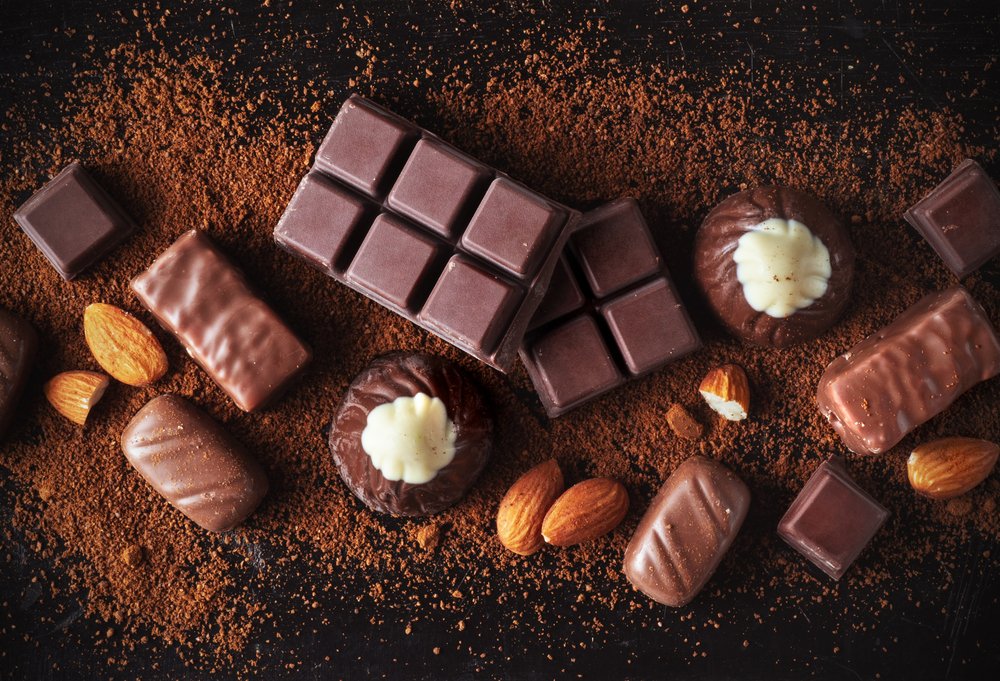 Assorted chocolate bars, truffles, and almonds on a bed of cocoa powder, creating a rich and indulgent treat scene.