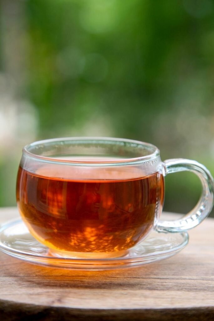 Clear glass cup of tea on wooden table with blurred green scenery background.