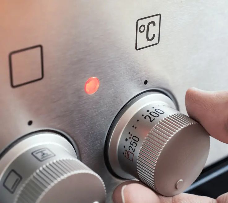 Hand adjusting oven temperature dial to 200°C with red indicator light on.