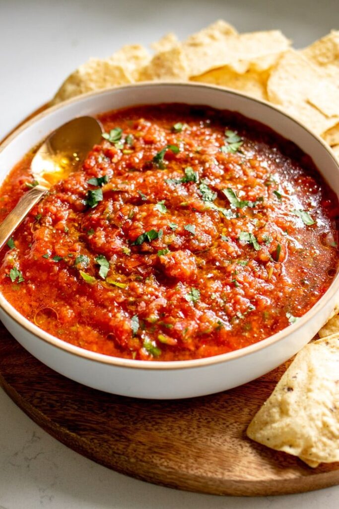 Bowl of fresh homemade salsa with cilantro garnish, served with tortilla chips on a wooden board.