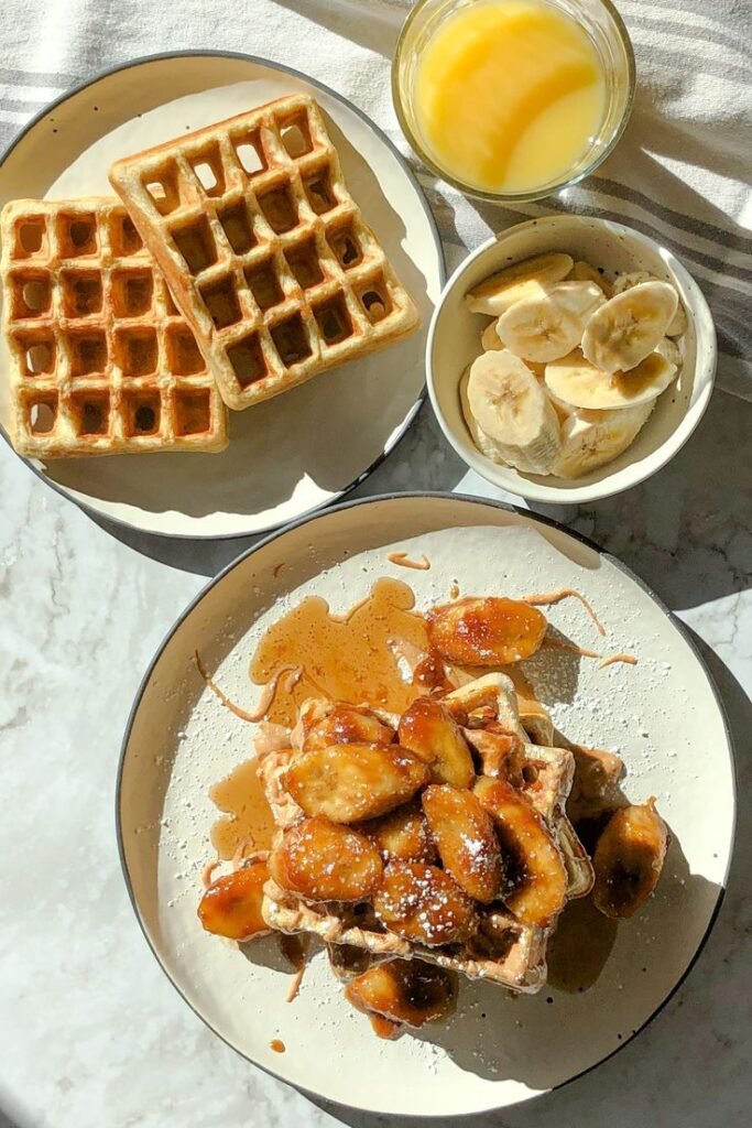 Delicious waffles topped with caramelized bananas, served with fresh banana slices and orange juice. Perfect breakfast!