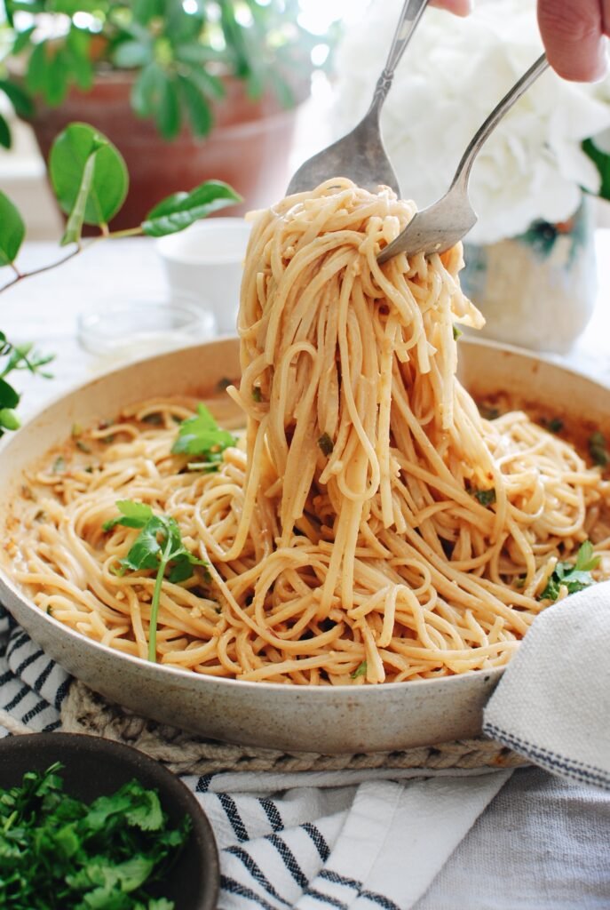 Fresh spaghetti being served from a skillet with herbs; delicious homemade pasta dish.