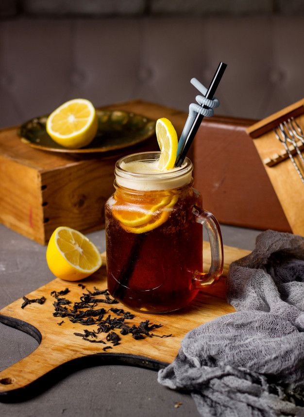 Refreshing iced tea with lemon slices in a mason jar, garnished with a straw on a rustic wooden board.