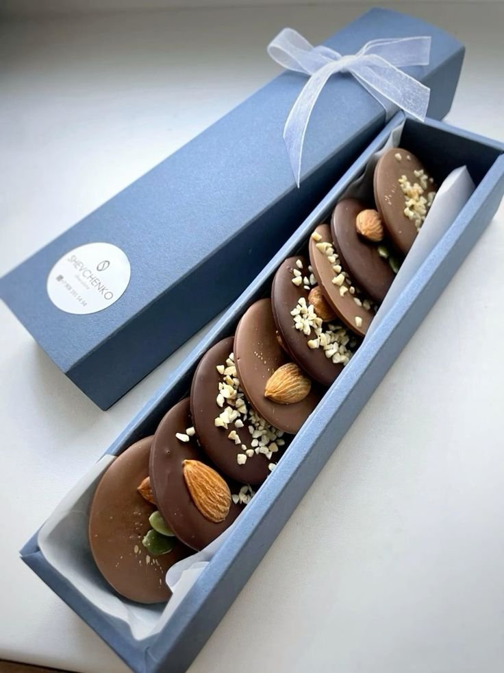 Box of gourmet chocolates topped with almonds and nuts in elegant packaging. Perfect gift choice.