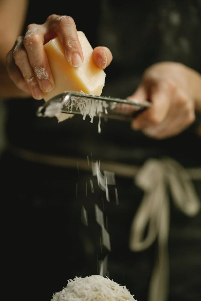 Hand grating cheese over a dish in a kitchen setting for culinary preparation.