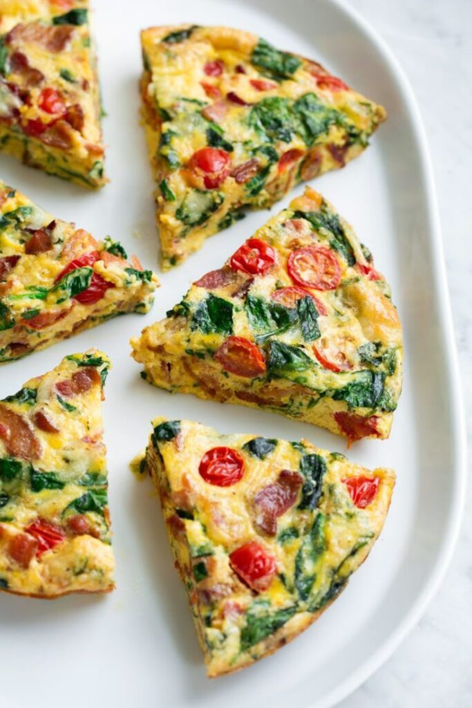 Slices of vegetable frittata with spinach and cherry tomatoes on a white plate.