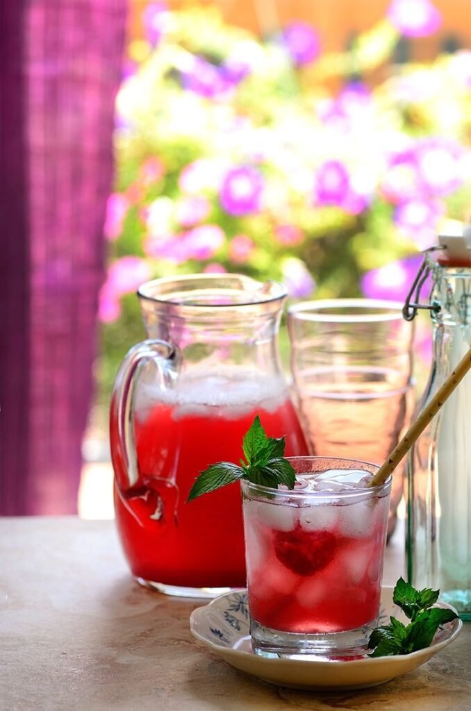 Refreshing raspberry lemonade with mint in glass and pitcher, set against a floral background.