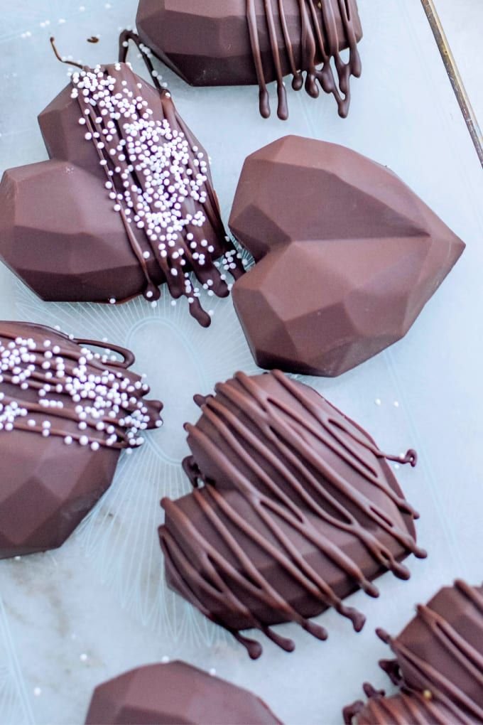 Geometric heart-shaped chocolates with drizzles and sprinkles on a tray. Perfect for Valentine's Day treats.