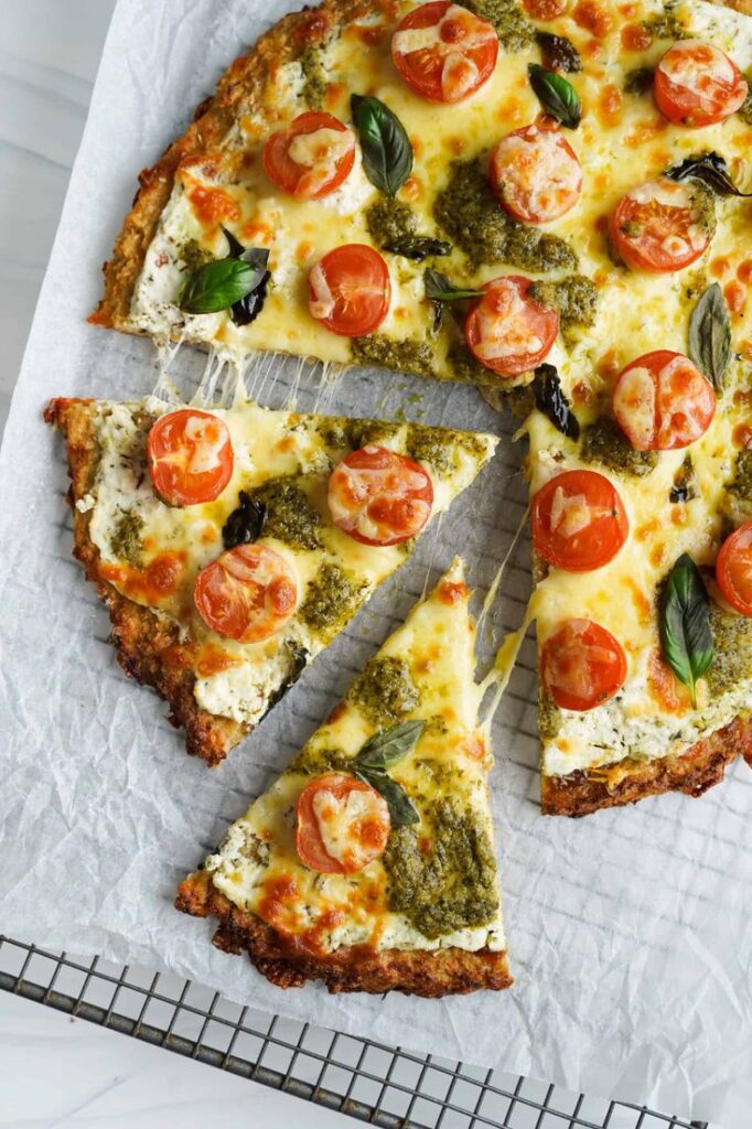 Cauliflower crust pizza topped with cherry tomatoes, basil, and pesto on parchment paper, delicious and healthy.
