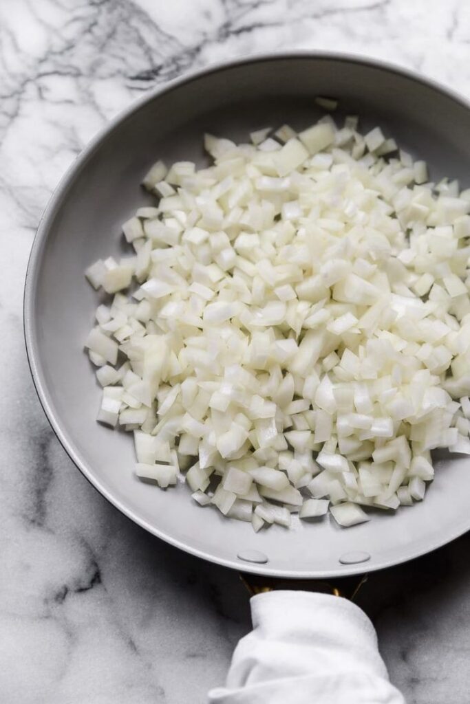 Diced onions in a frying pan on a marble counter, ready for cooking.
