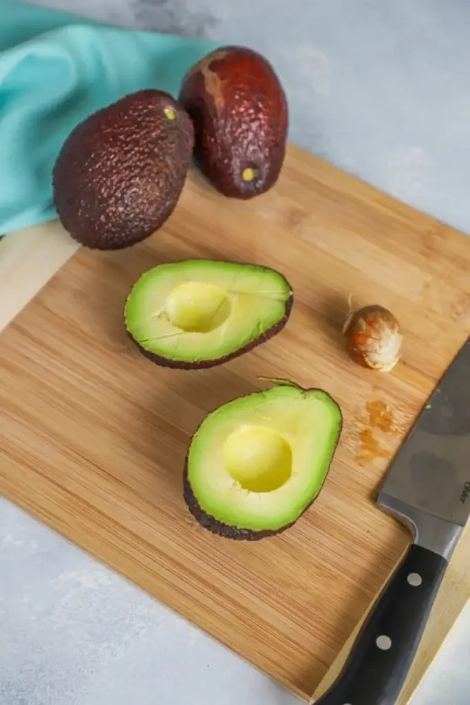 Sliced avocado on a cutting board with whole avocados and knife nearby, ready for a fresh recipe.