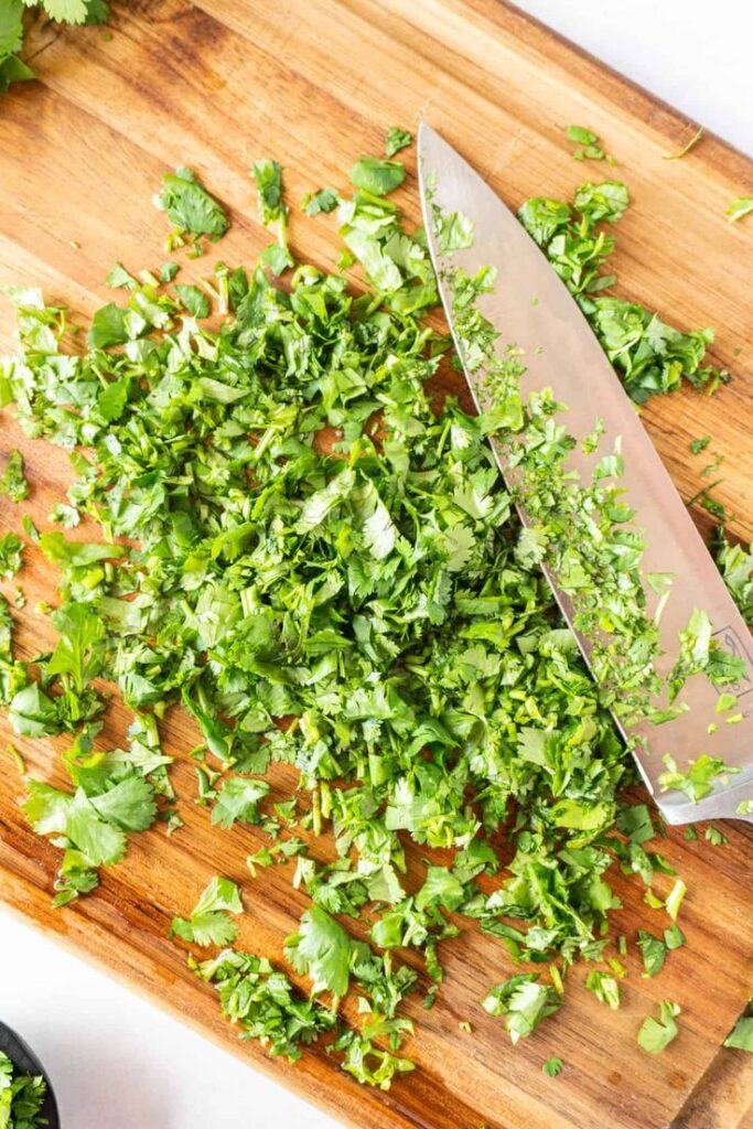 Chopped cilantro on a wooden cutting board with a knife, fresh herbs for cooking.