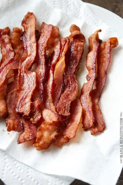 Crispy cooked bacon strips on a plate with paper towel, perfect breakfast side dish.