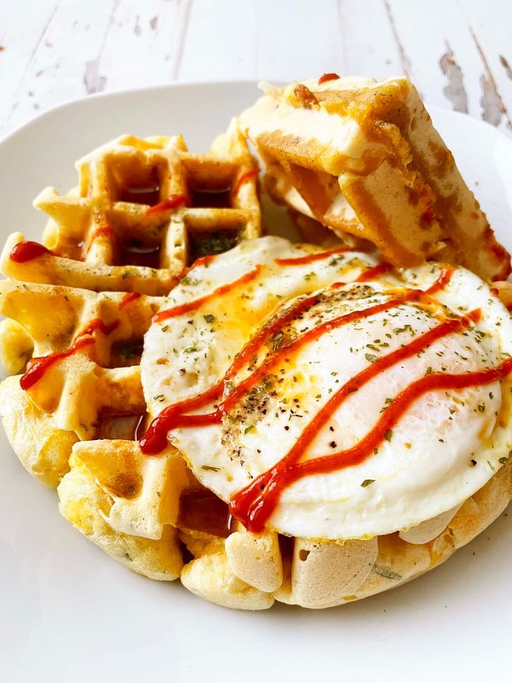 Waffles topped with a fried egg and drizzled with hot sauce on a white plate, perfect breakfast treat.