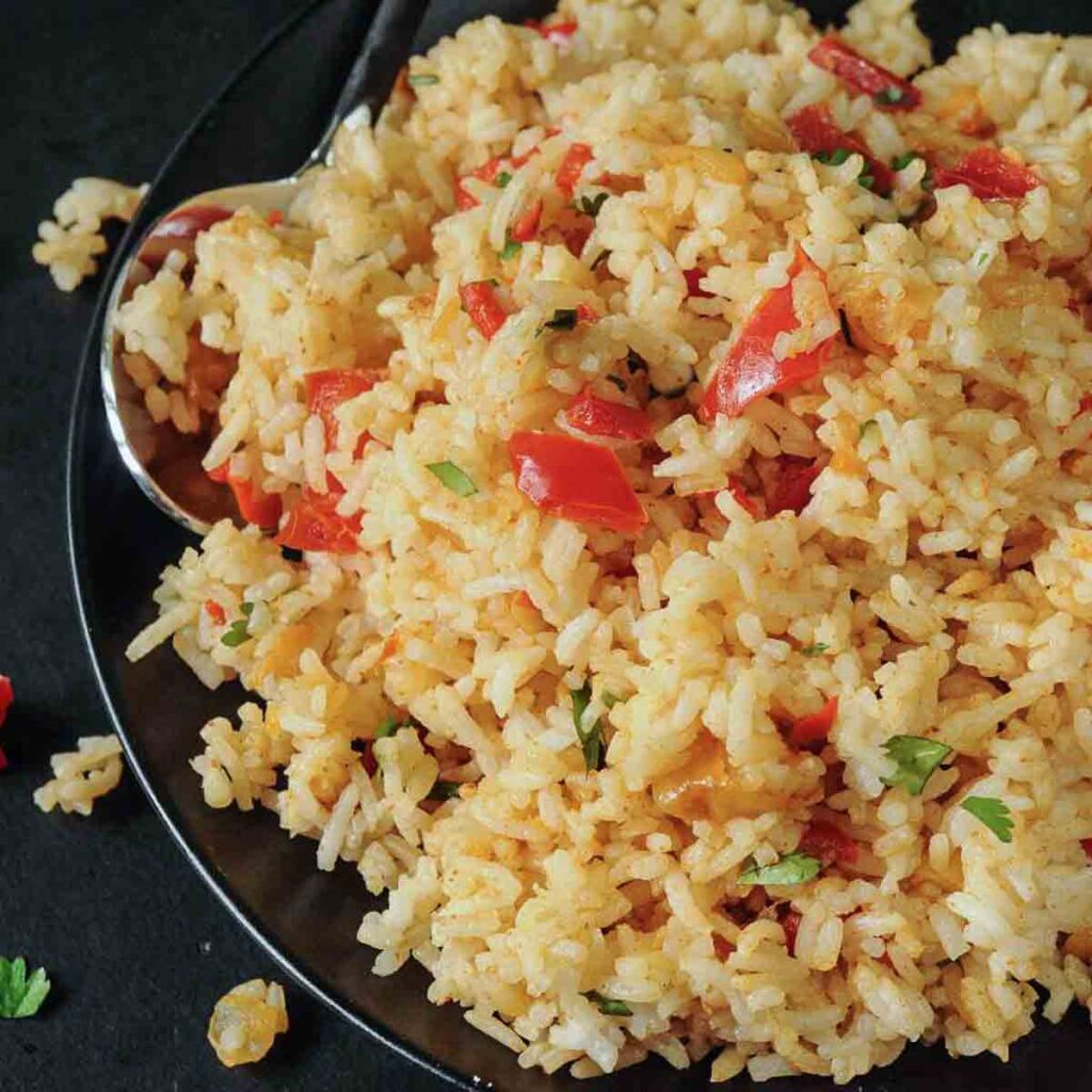 Delicious spicy rice dish with red peppers and herbs on a black plate, perfect for a flavorful meal.