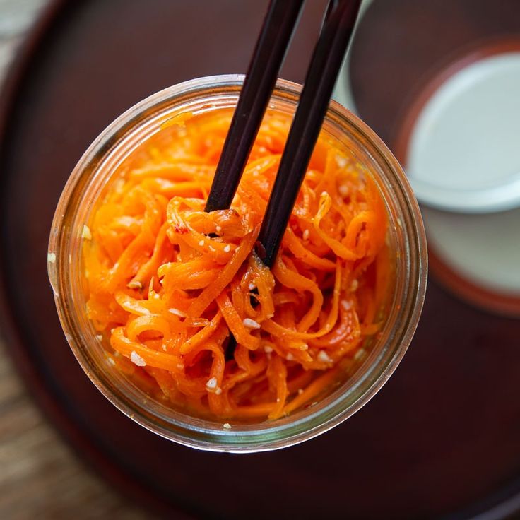 Chopsticks holding Korean-style carrot salad in a jar, top view on a wooden table for a delicious appetizer.