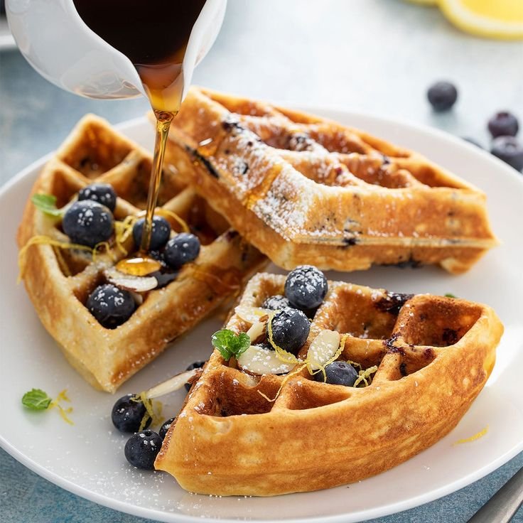 Waffles topped with blueberries and syrup, garnished with mint and powdered sugar on a white plate.