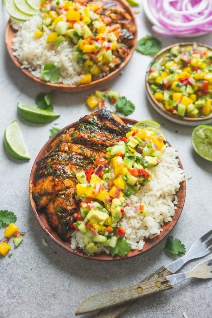 Grilled chicken with mango avocado salsa and rice in a wooden bowl, garnished with lime and cilantro.